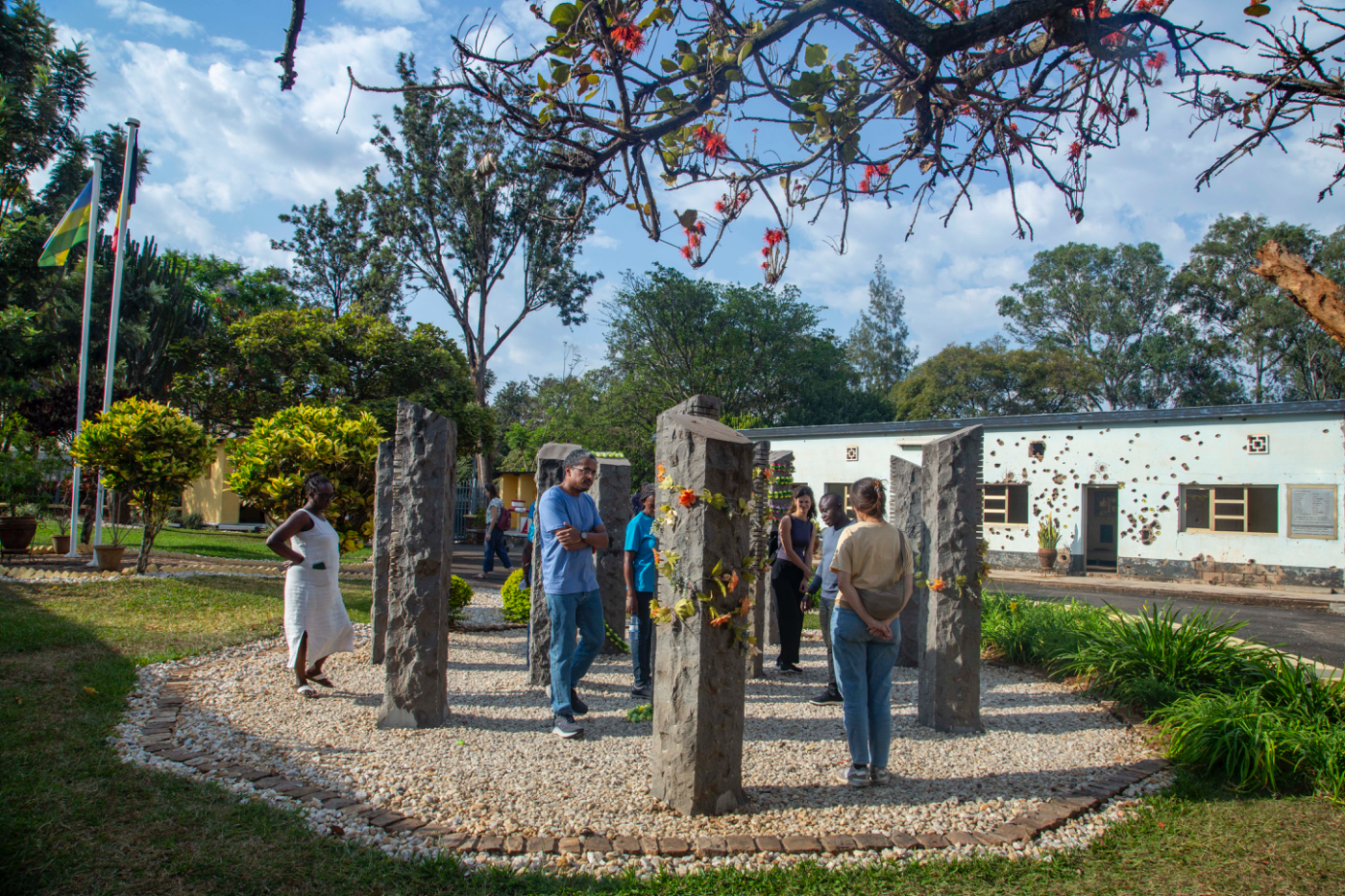 Guests among the ten stone pillars of the Belgian Peacekeepers Memorial at Camp Kigali, with the bullet-scarred building behind, on the Kigali Past & Present tour